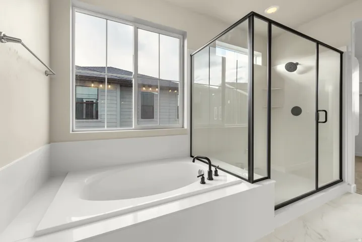 Soaking tub with black fixtures, framed by a large window