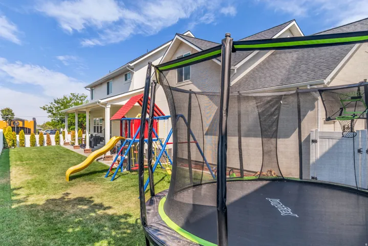 Expansive backyard featuring a manicured lawn, white privacy fencing, and a covered patio with columns