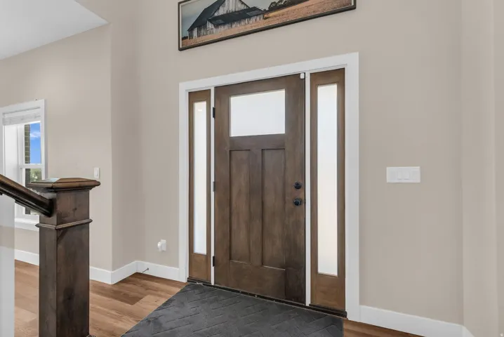 Wood-finish flooring, staircase with dark wood newel post, and a paneled entry door with frosted sidelights