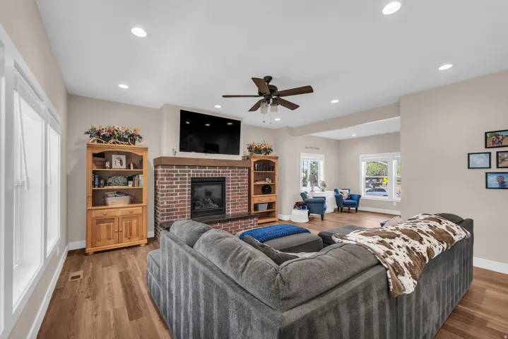 Brick fireplace with a stone hearth, wood-finish flooring, recessed lighting, and a ceiling fan