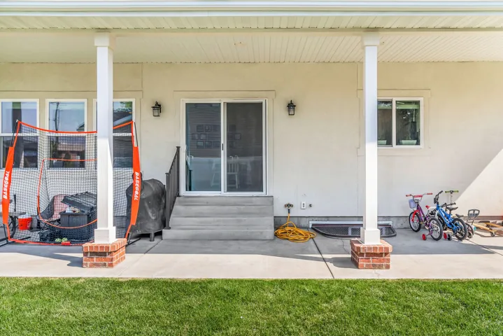 Expansive covered patio featuring concrete flooring, white support columns with brick bases, and a sliding glass door