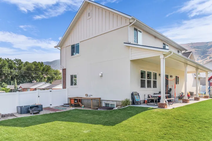 Expansive lawn area with a white privacy fence, multi-paned windows, and a covered patio supported by columns with brick bases