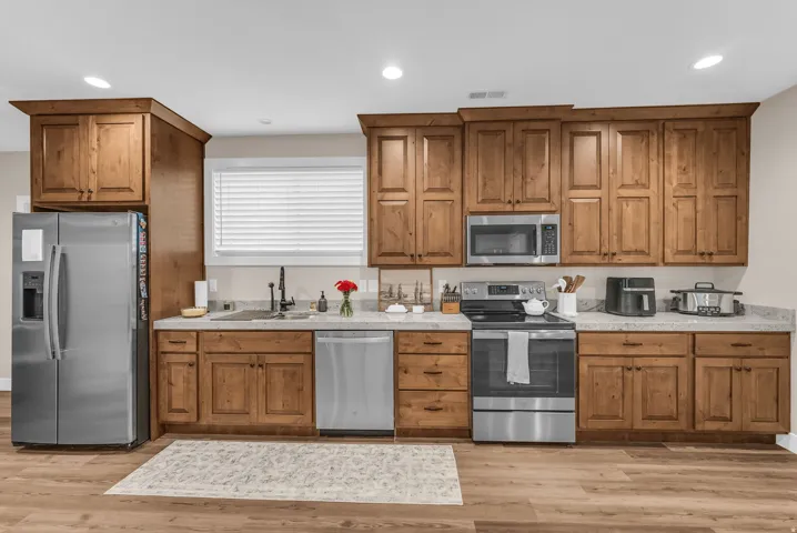 Basement kitchen featuring wood-finish cabinetry, stainless steel appliances, light-toned countertops, and wood-finish flooring