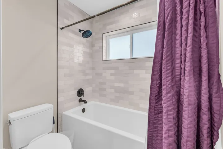 White subway tile shower surround with integrated window, deep soaking tub, and matte black fixtures