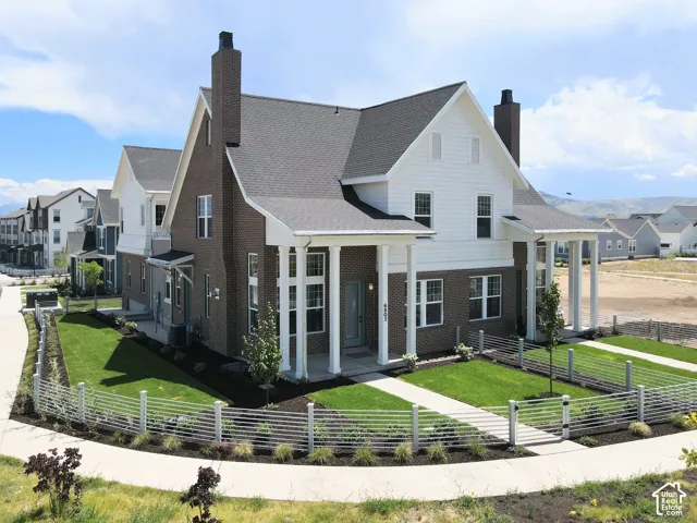 Brick and white siding exterior featuring a covered porch with white columns, dark shingle roof, twin chimneys, and a fenced front yard with a paved walkway