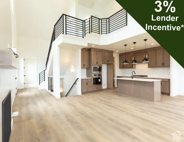 Open-concept living space with wood-finish flooring, a contemporary kitchen featuring integrated appliances, a central island, and pendant lighting