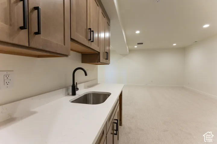 Integrated wet bar featuring a stainless steel undermount sink, matte black faucet, light wood-finish cabinetry with black hardware, and a white countertop