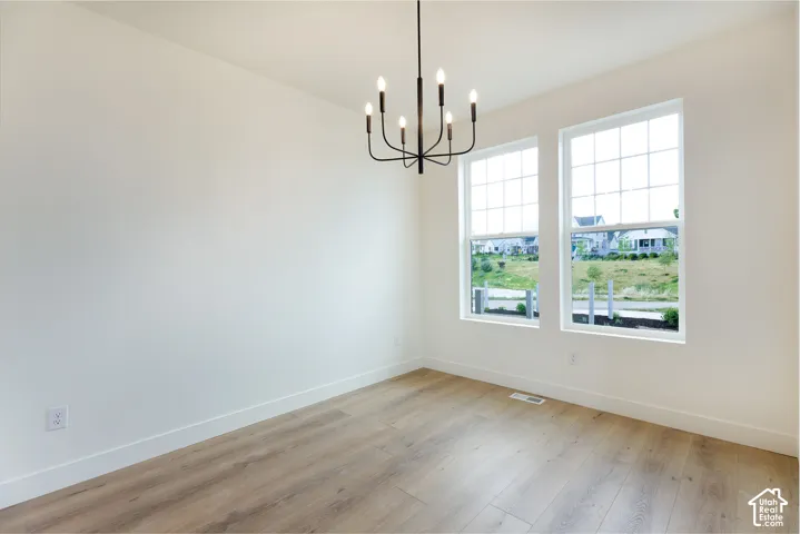 Room featuring light wood-finish flooring, two large grid-pattern windows, a contemporary black chandelier, white walls, and white baseboards