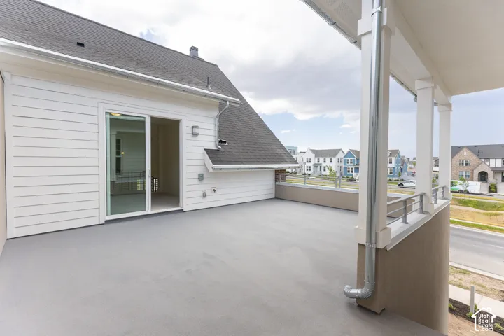 Expansive exterior balcony featuring a sliding glass door entry, white horizontal siding, a protective railing, and a dark shingle roof