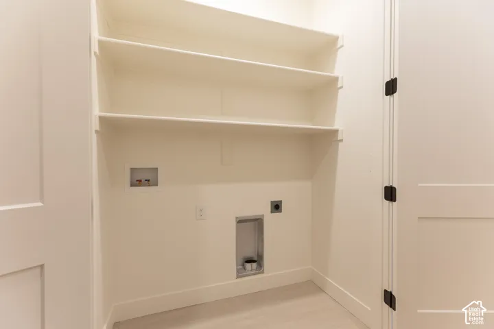 Dedicated laundry area featuring built-in shelving, plumbing hookups, and electrical outlet