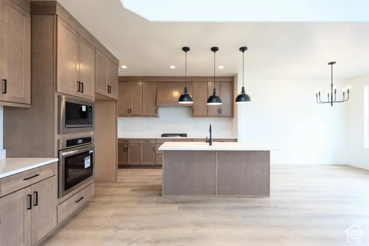 Kitchen featuring wood-finish cabinetry, stainless steel appliances, a center island with pendant lighting, and wood-finish flooring