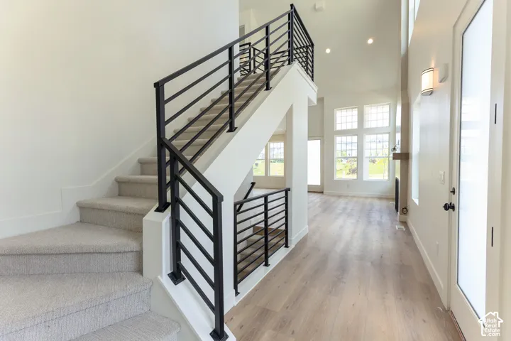 Carpeted staircase with black metal railings, vaulted ceiling, recessed lighting, wood-finish flooring, and large windows