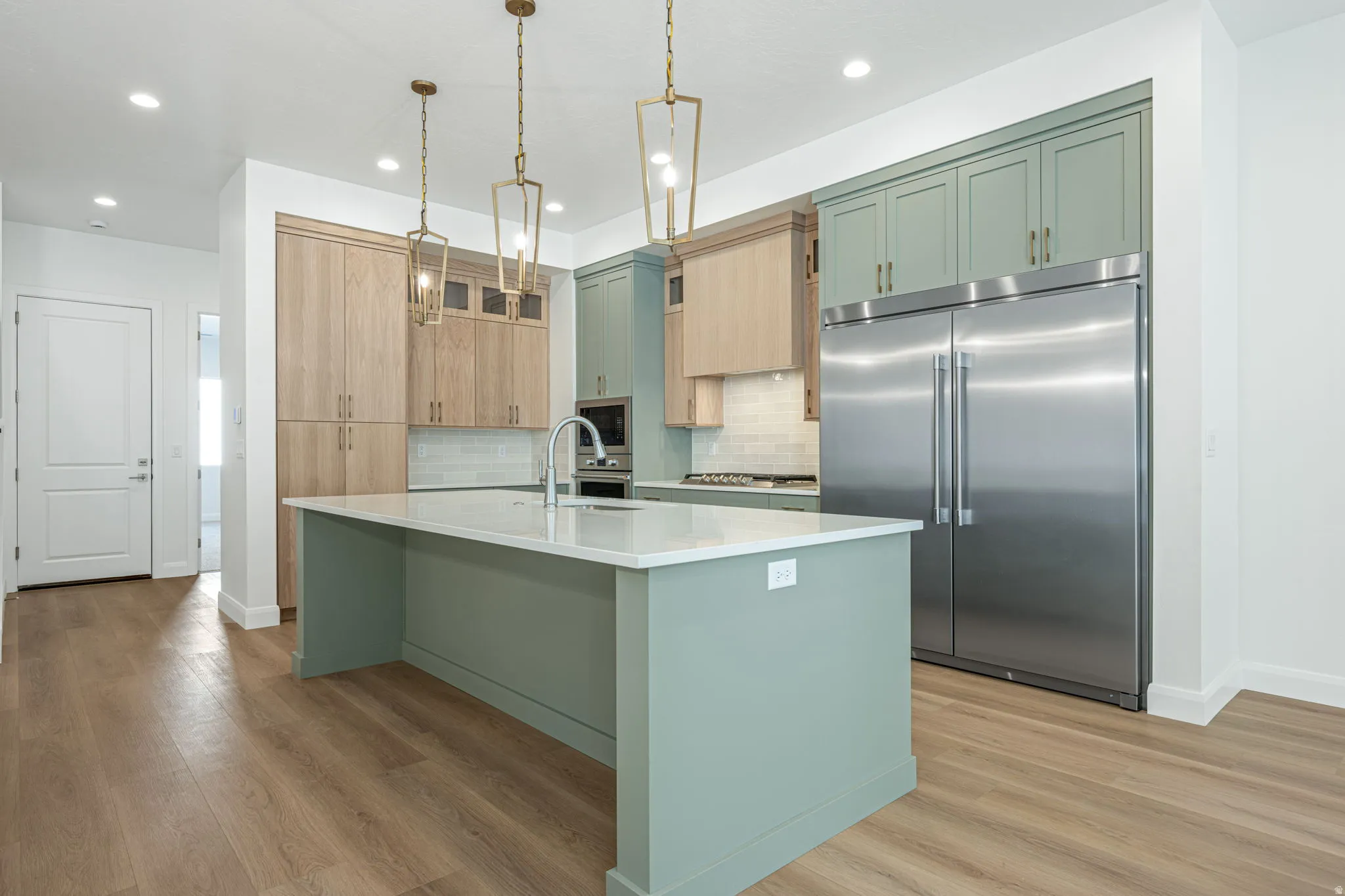 Kitchen featuring a large center island with a light-colored countertop, wood-finish flooring, two-tone cabinetry, and stainless steel appliances