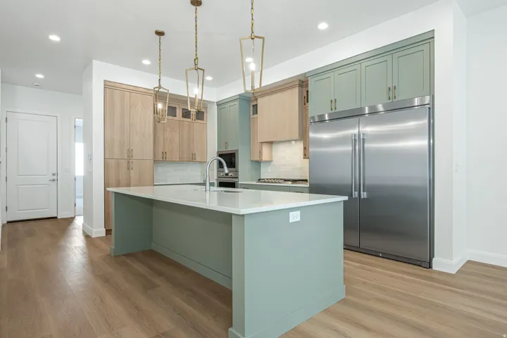 Kitchen featuring a large center island with a light-colored countertop, wood-finish flooring, two-tone cabinetry, and stainless steel appliances