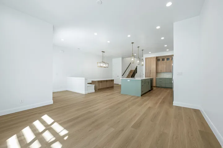 Wood-finish flooring throughout, recessed ceiling lighting, kitchen island with pendant lighting, light wood-finish cabinetry, and a subway tile backsplash