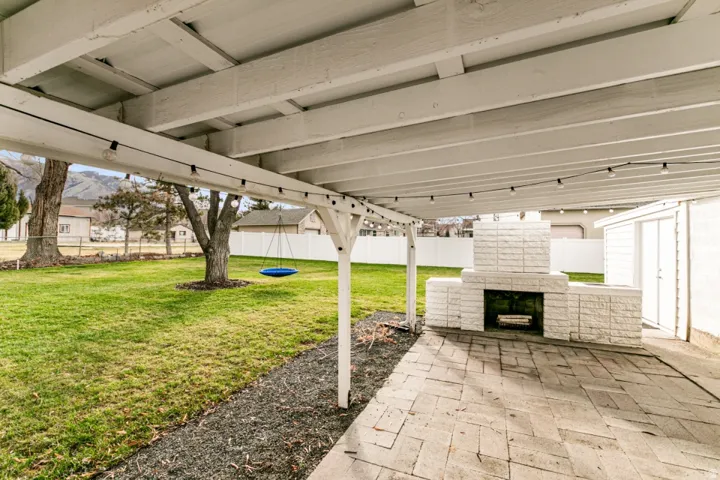 Expansive covered patio with white structural columns and coffered ceiling, featuring a paver surface and integrated outdoor fireplace