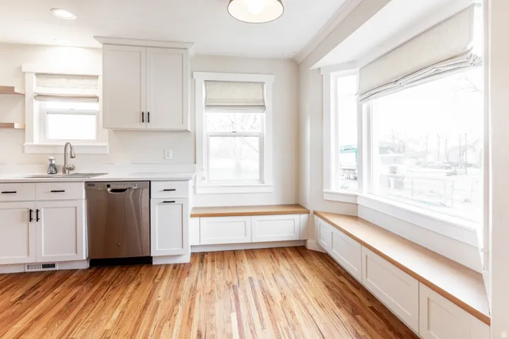 Wood-finish flooring, white cabinetry, stainless steel dishwasher, and built-in window seating with storage