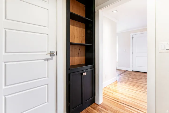 Hallway featuring warm wood-finish flooring, white panel doors, and a custom black built-in cabinet with open shelving and lower storage cabinetry