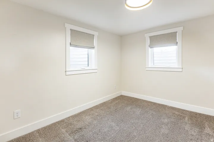 Neutral-toned walls, two windows with window treatments, and carpeted flooring
