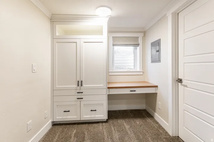 Dedicated home office or bonus room featuring custom cabinetry with dual upper cabinets and lower drawers, wood-finish desk surface, recessed lighting, and large window with natural light