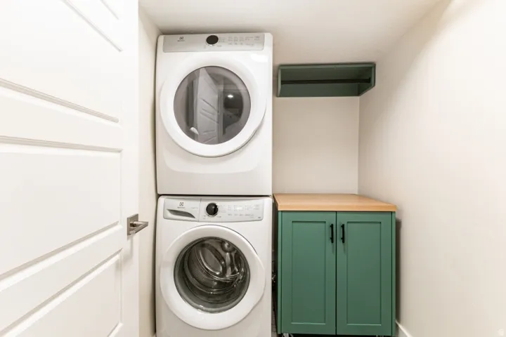 Dedicated laundry area featuring a stacked washer and dryer, painted shaker-style cabinetry with a wood-finish countertop, and an overhead open shelf