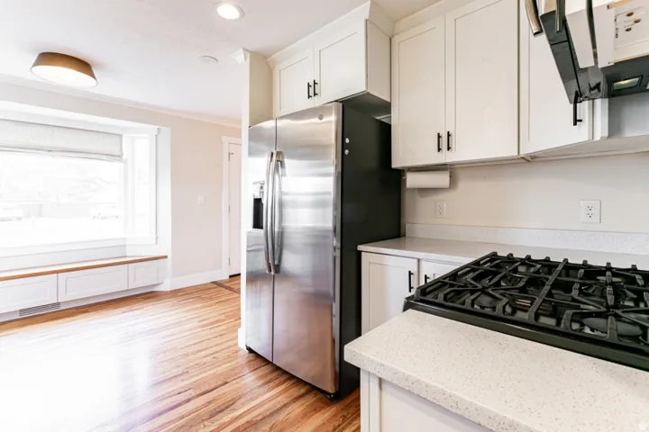 Stainless steel refrigerator, white cabinetry with black hardware, wood-finish flooring, built-in window seating, and a gas cooktop with a griddle feature