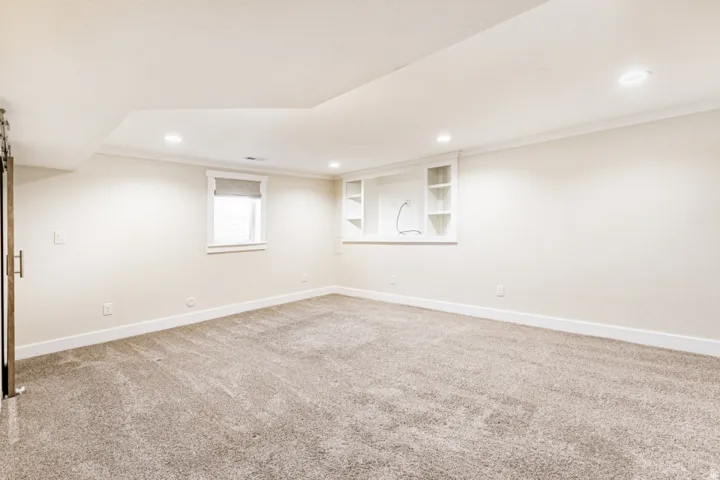 Recessed lighting, light-toned carpeting, built-in shelving, white trim, and a window with a roller shade
