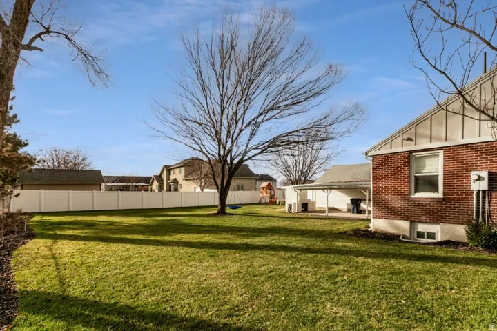 Expansive green lawn, mature trees, white privacy fencing, brick exterior, and a covered carport