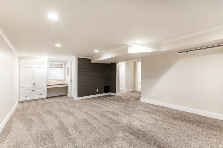 Expansive carpeted area featuring recessed lighting, a built-in desk with window, white cabinetry, and shiplap accent wall