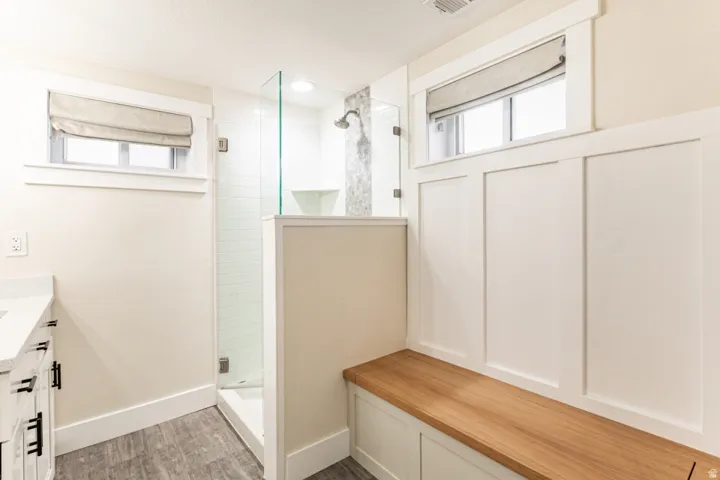 Glass-enclosed shower with subway tile, built-in wooden bench, board and batten wall detailing, and a vanity featuring a white countertop and dark hardware
