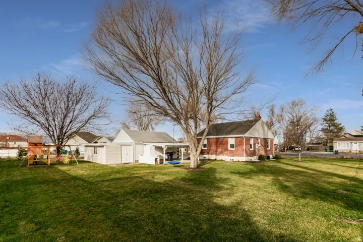 Spacious residential property featuring a brick exterior, detached garage with white finish, and expansive manicured lawn anchored by mature shade trees