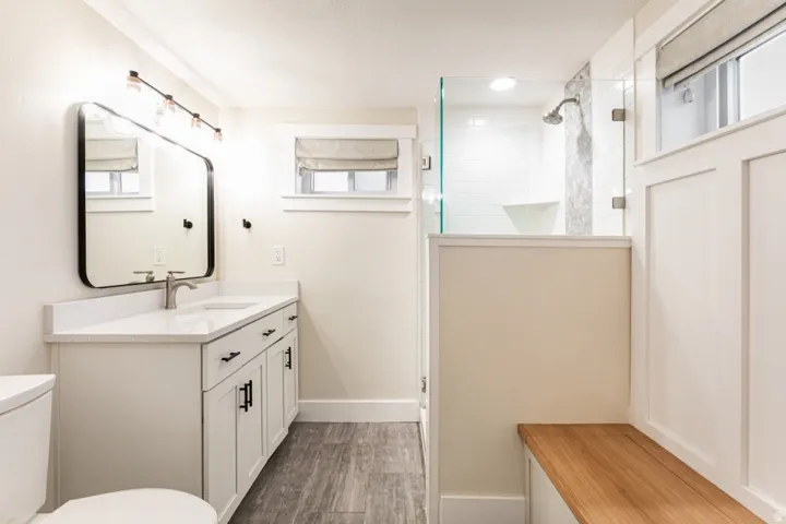 Vanity with a white countertop and undermount sink, wood-finish flooring, glass-enclosed shower, and built-in wood bench