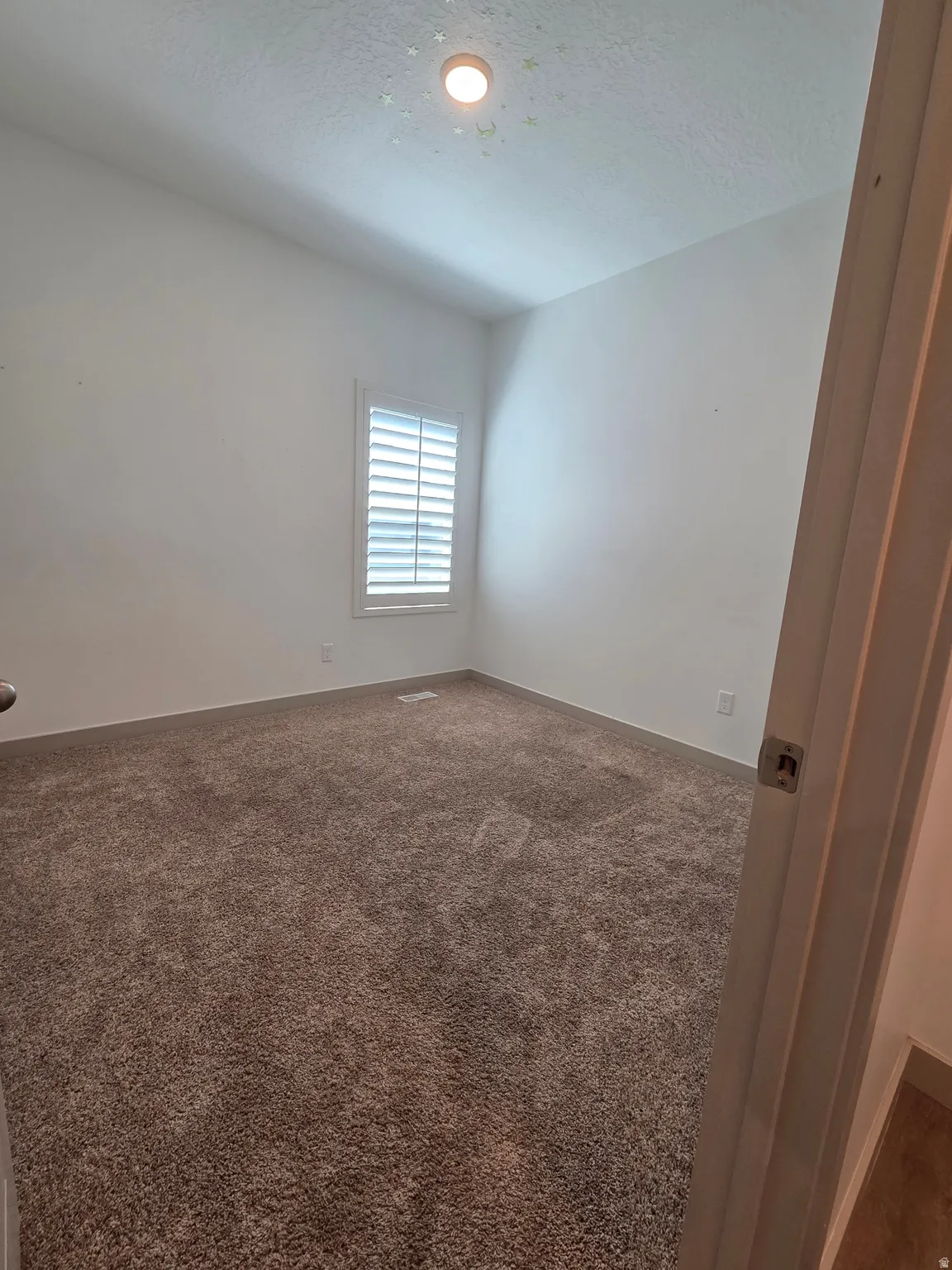 Plush carpet flooring, white walls, and a window with plantation shutters