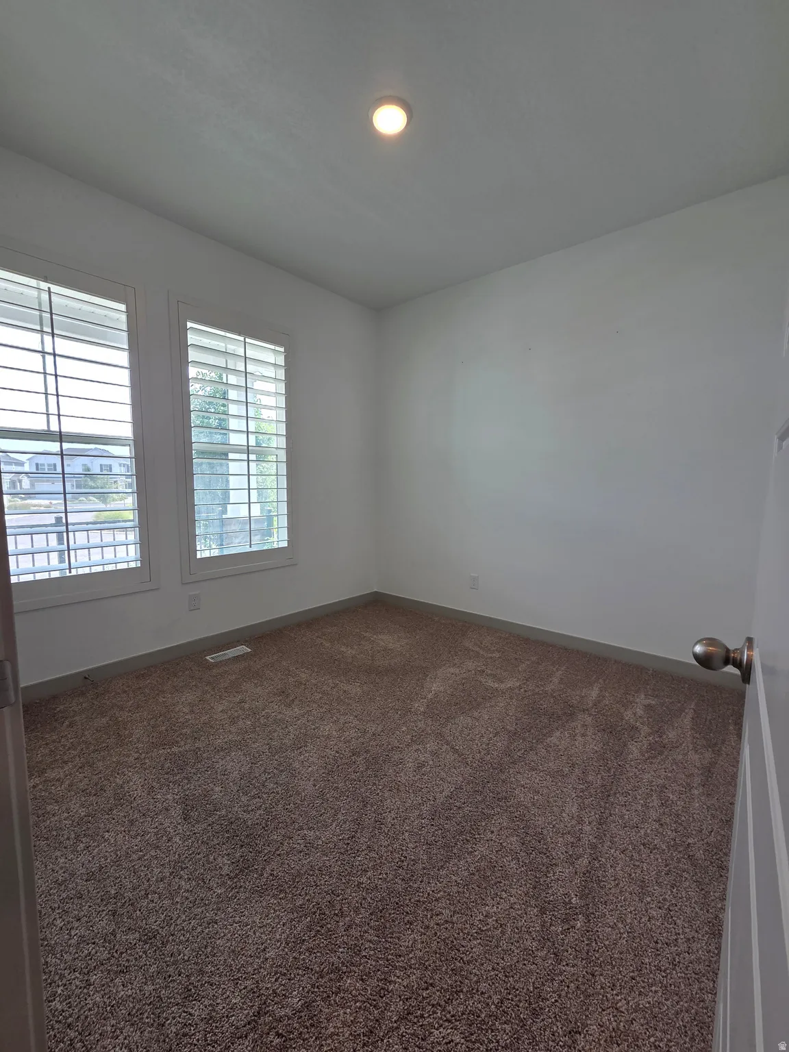 Bright corner bedroom with dual glass doors featuring integrated blinds, neutral wall finishes, and plush carpeting throughout
