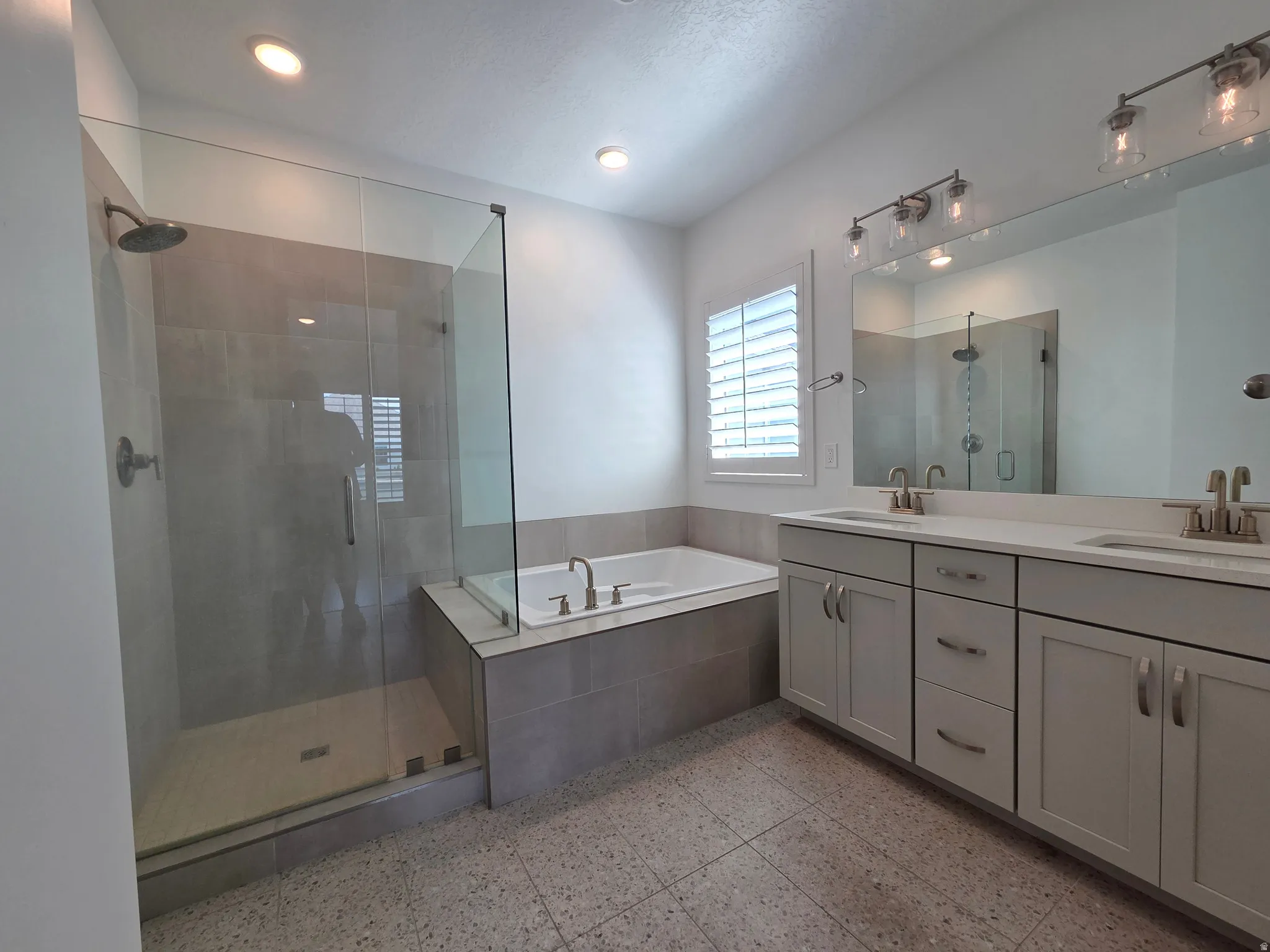 Spacious bathroom featuring a glass-enclosed shower, built-in soaking tub, dual vanity with undermount sinks, large mirror, and recessed lighting