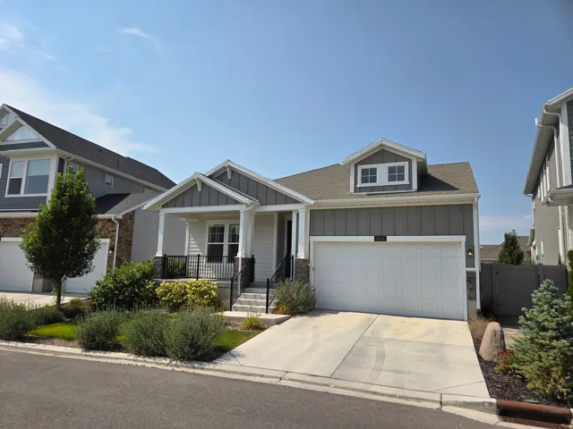 Craftsman-style exterior with a covered porch, attached garage, dormer window, and mature landscaping