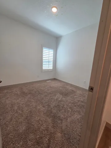 Plush carpet flooring, white walls, and a window with plantation shutters