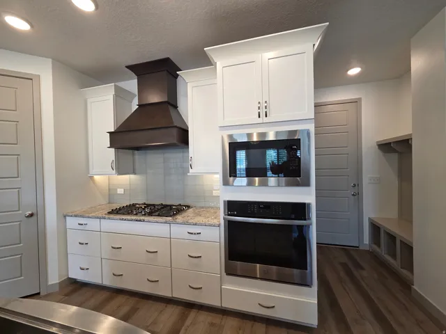 White cabinetry, stainless steel appliances, gas cooktop, built-in oven and microwave, and wood-finish flooring