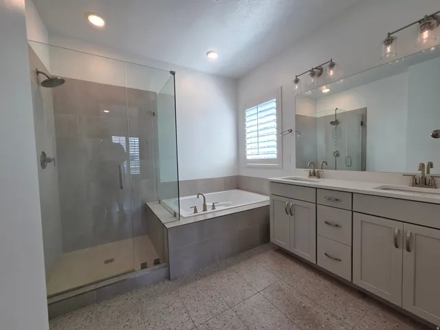 Spacious bathroom featuring a glass-enclosed shower, built-in soaking tub, dual vanity with undermount sinks, large mirror, and recessed lighting