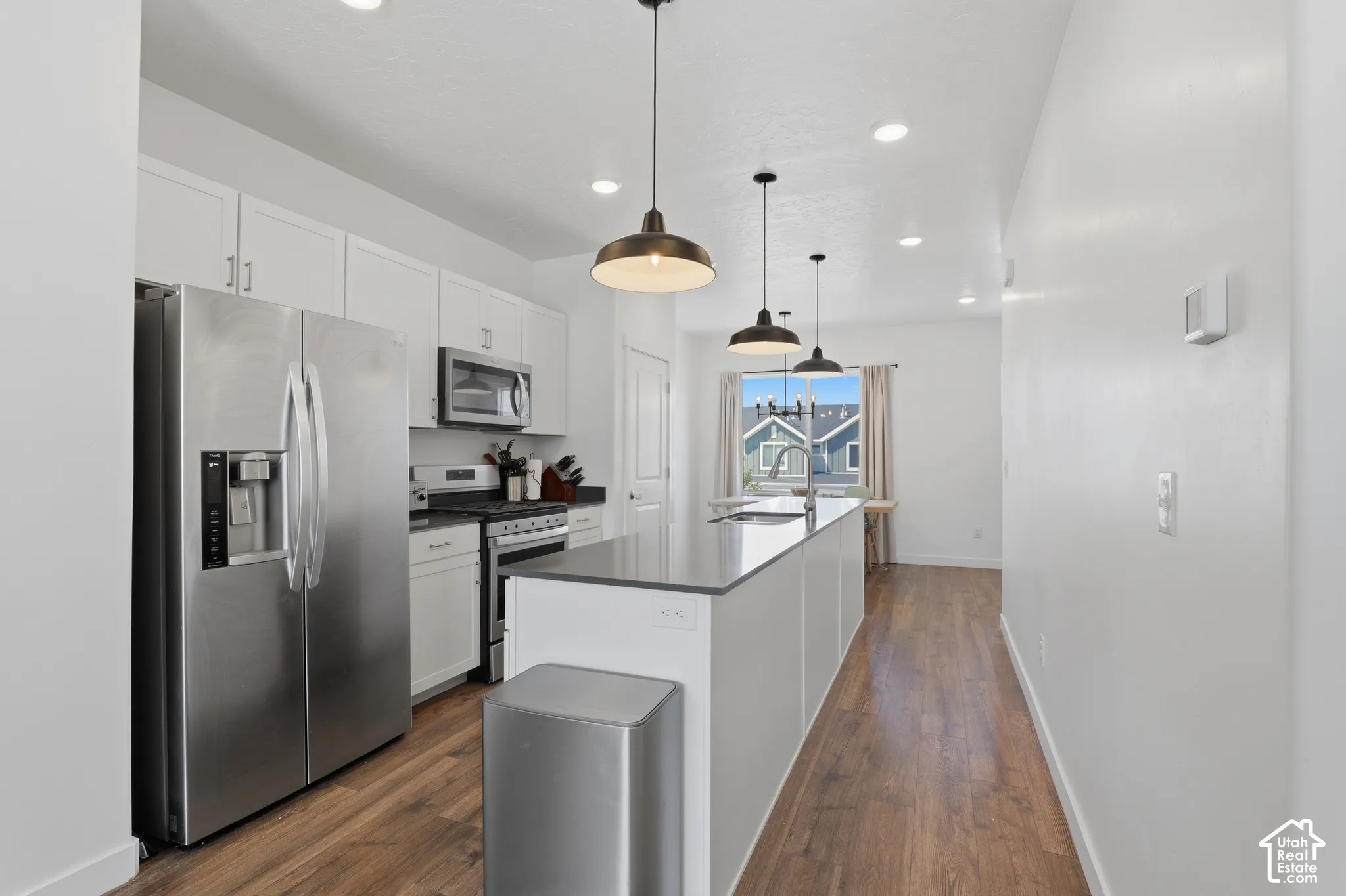 Modern kitchen featuring stainless steel appliances, white cabinetry with ample storage, a central island with prep space, wood-finish flooring throughout, and pendant lighting suspended from a vaulted ceiling with recessed fixtures