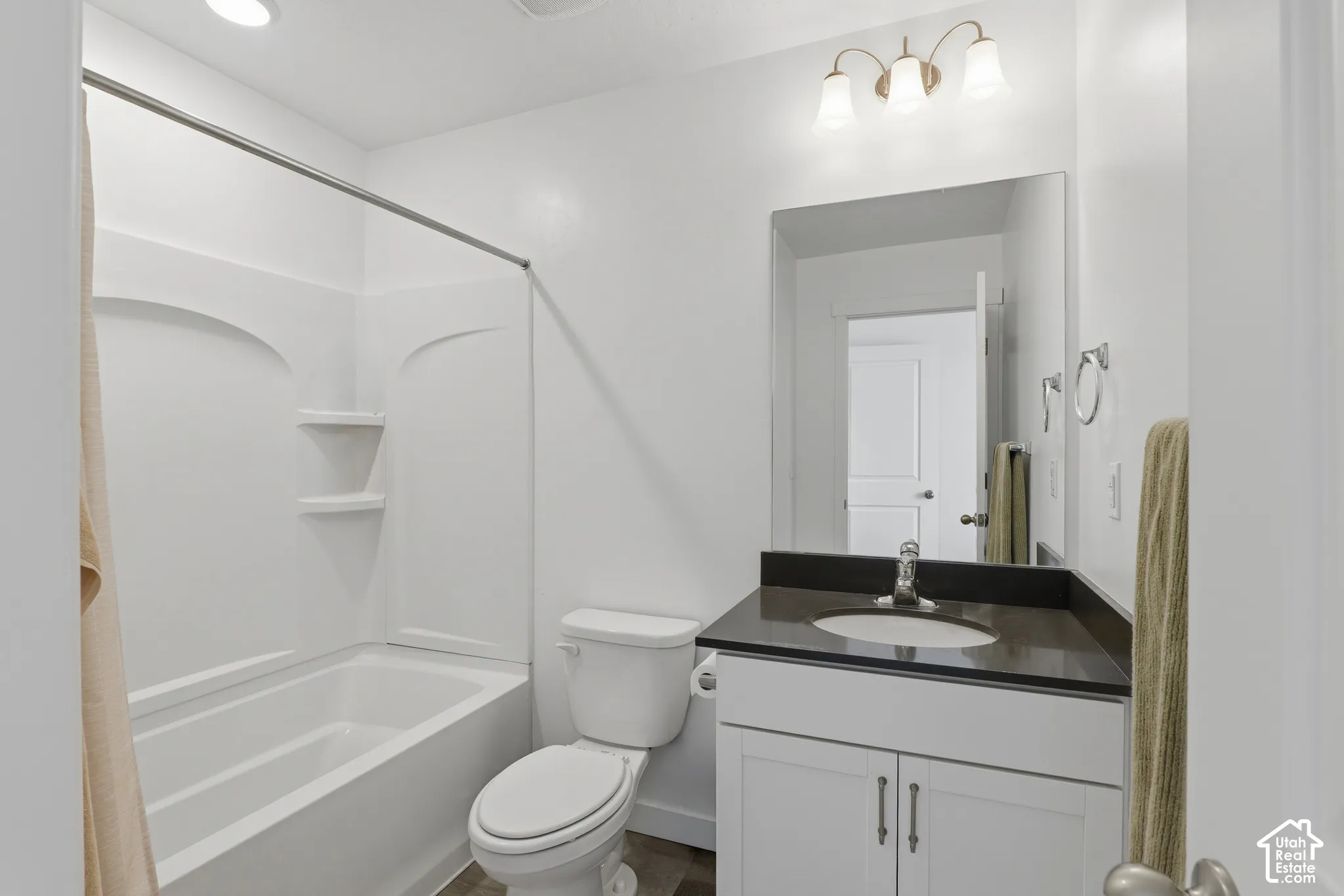 White vanity with dual-door cabinetry, dark countertop, and integrated sink