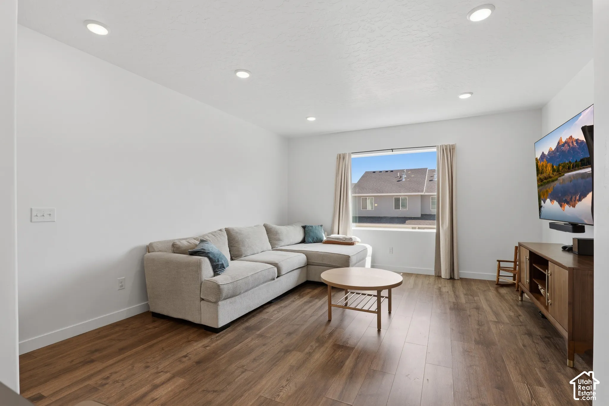 Recessed lighting illuminates this bright interior featuring wood-finish flooring and a window with light-filtering drapes