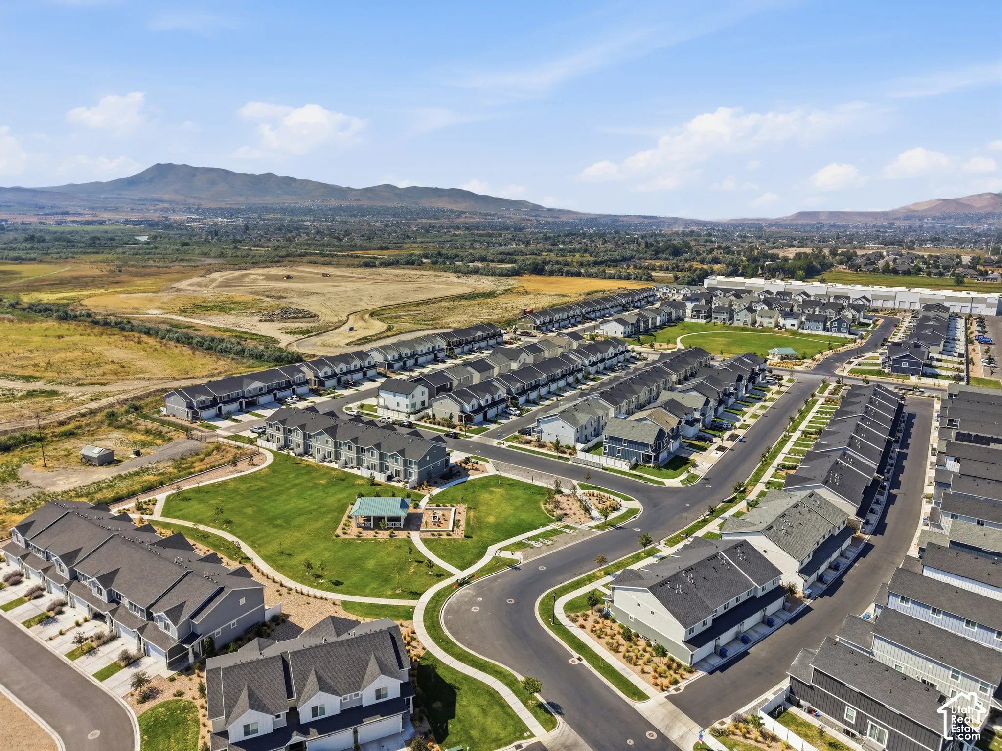 Residential development featuring multiple townhome-style residences, paved streets, landscaped common areas with green spaces, and mountain scenery