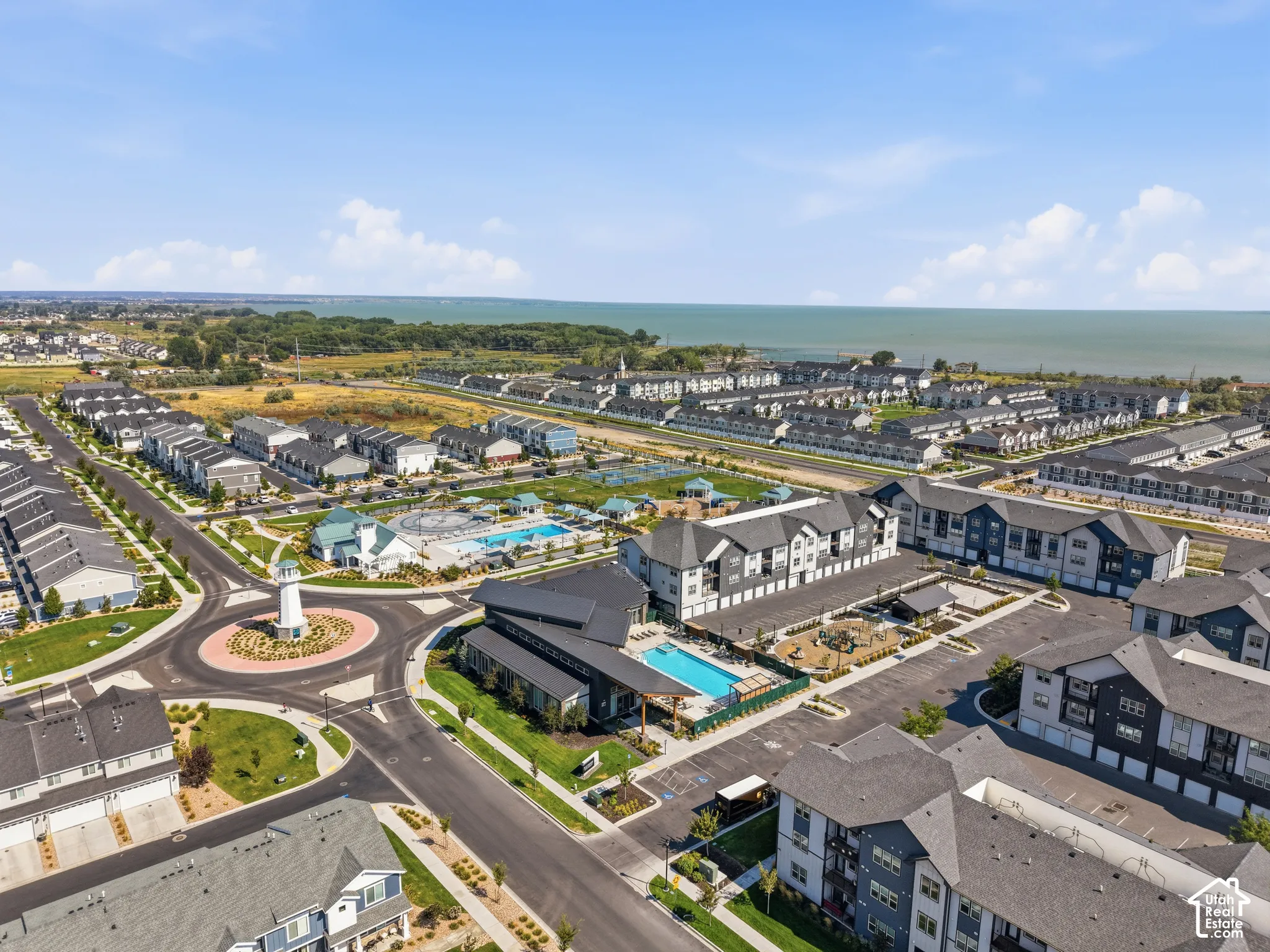 Expansive community with varied residential structures, multiple swimming pools, a central roundabout, and a prominent water feature in the background