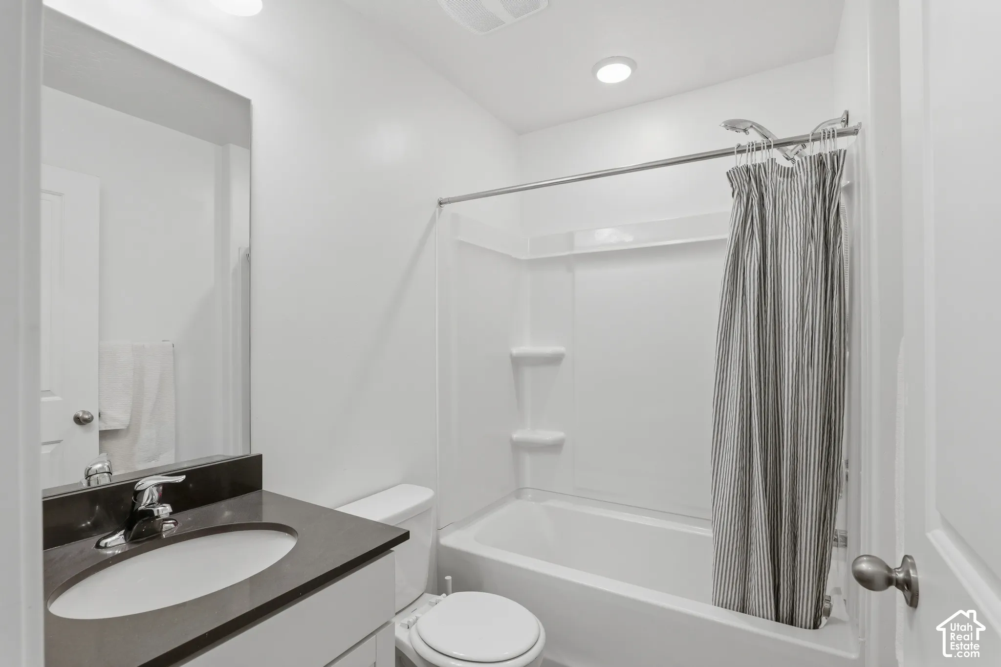Bathroom featuring a white vanity with a dark countertop, an undermount sink, a chrome faucet, and a shower-over-tub combination with a white surround