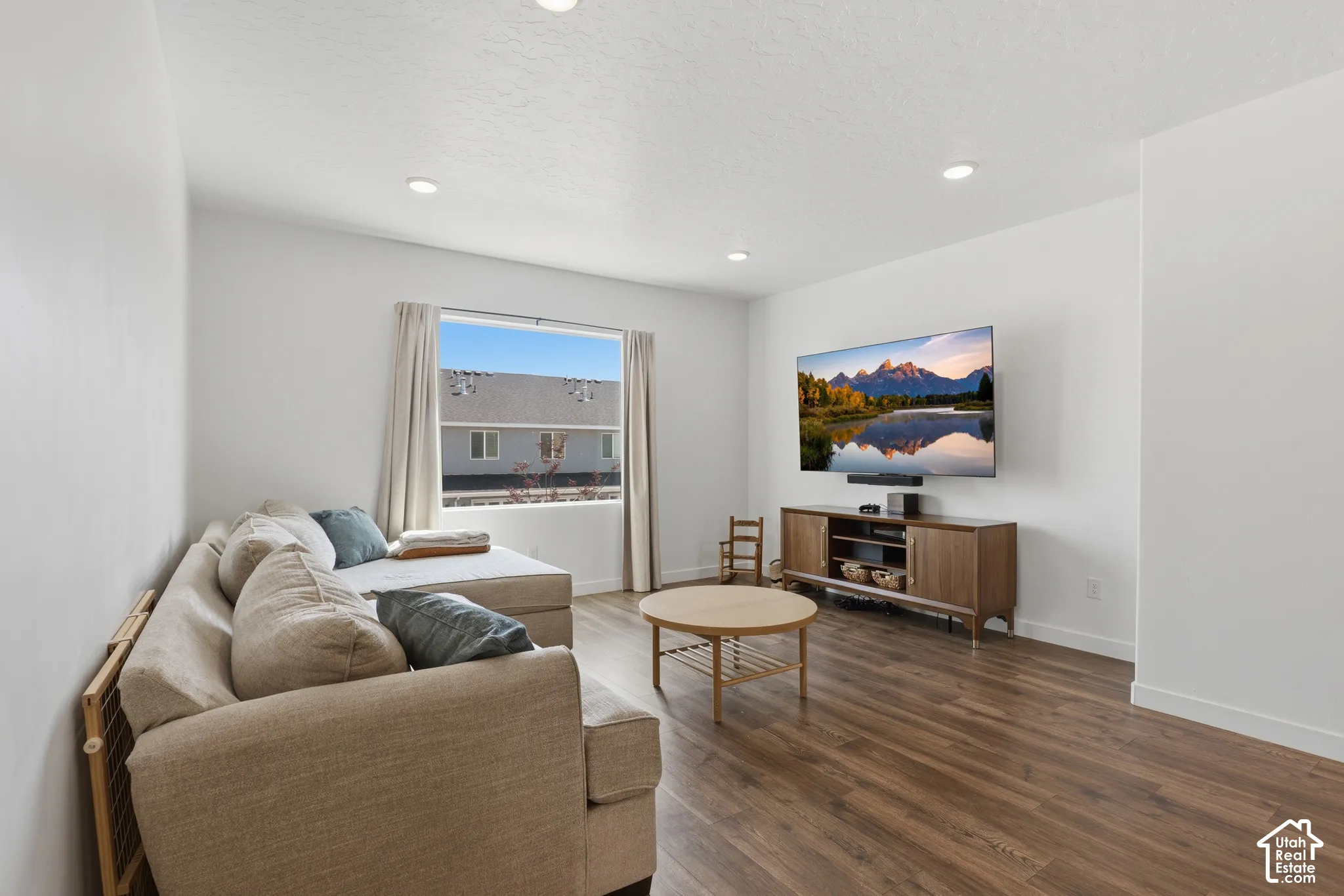 Bright, open-concept living area featuring recessed ceiling lighting, wood-finish flooring throughout, and large windows framed with neutral drapery