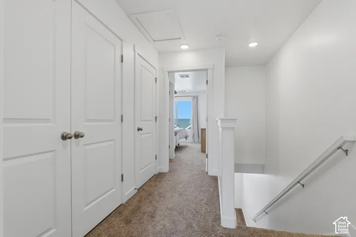 Neutral wall paint, recessed lighting, white doors with brushed nickel hardware, carpeted flooring, and a white balustrade with a metal handrail