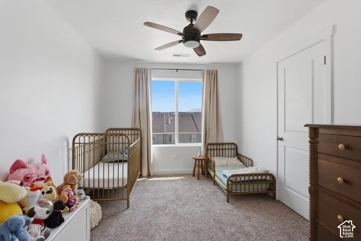 Bright secondary bedroom featuring hardwood crib and toddler bed frames, carpeted flooring, ceiling fan with remote control, glass sliding door with natural light, and ample closet storage with white trim