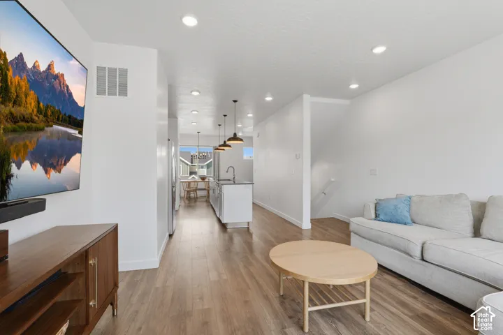 Recessed lighting throughout, wood-finish flooring, white walls, and a modern kitchen with a white island