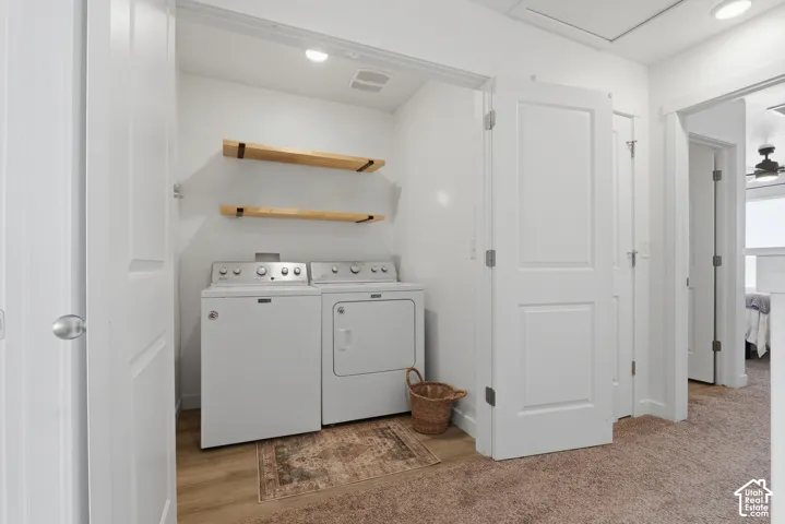 Dedicated laundry room featuring side-by-side washer and dryer appliances, wood-finish floating shelves for storage, recessed ceiling lighting, and wood-finish flooring throughout